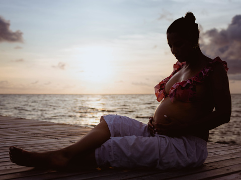 high contrast silhouette of pregnant woman sitting on pier with sea and sunset in background