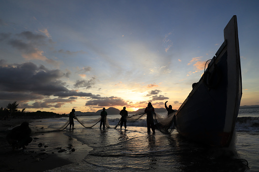 Banda Aceh 12/30/2021 Daily activities of Javanese village fishermen cleaning nets from fish and trash from the catch and putting them back into traditional wooden boats when the beautiful sun sets