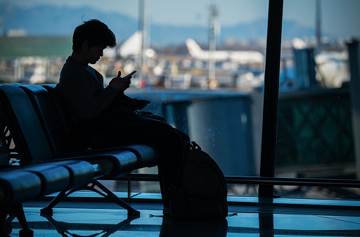 Silhouette of young man looking at mobile phone in airport
