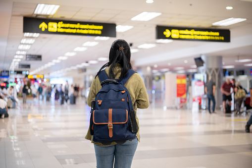 Back view image of an Asian female solo traveler or backpacker with her backpack is walking in the airport, finding her check in counter.