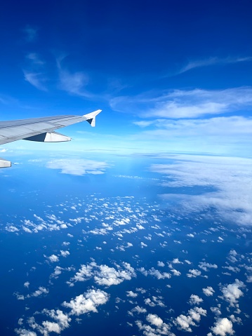 A portrait of vivid clear blue sky and a layer of white cloud on the bottom, with an air plane wing on the left side of picture.