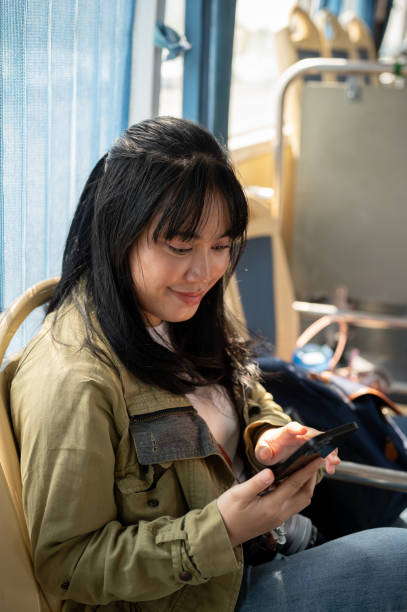 istock A smiling Asian female passenger is using her smartphone while sitting in a bus. 2024278669