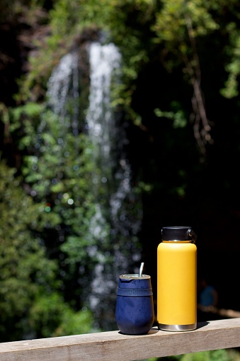 cup with mate and yellow thermos on a railing at the edge of a waterfall, vacation concept, outdoor activity