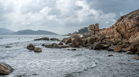 seascape of coastal panorama. Monumental granite boulders stand resilient against crashing waves, set beneath dramatic, cloud-filled sky. landscape captivates with its vastness and natural spectacle
