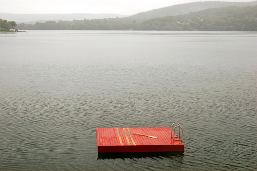 A small red platform with an oar sits in the middle of a foggy lake