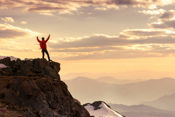 Hiker silhouette is standing in winner pose at mountain top against sunset sky