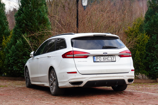 Studzienno, Poland – February 15, 2024: White car parked near trees and brick wall