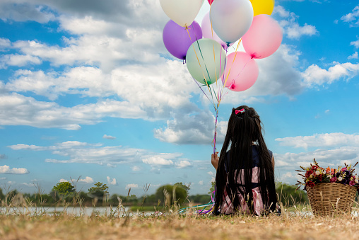 Cheerful cute girl holding balloons running on green meadow white cloud and blue sky with happiness. Hands holding vibrant air balloons play on birthday party happy times summer on sunlight outdoor