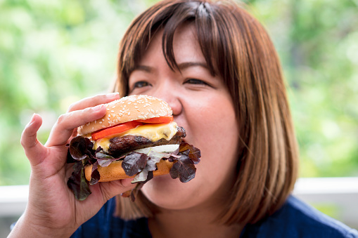 Hungry overweight woman holding hamburger on wooden plate after delivery man delivers foods at home. Concept of binge eating disorder BED and Relaxing with Eating junk food.