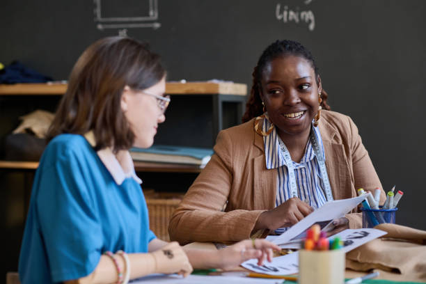 Teacher talking to student during sewing class stock photo