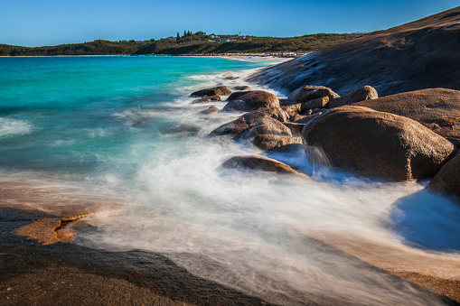 Slow shutter coastal scene with aqua marine blue ocean waves washing gently around rocks. Western Australia.