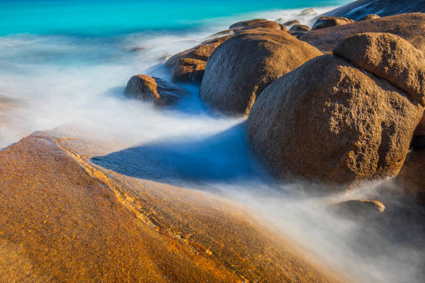 Slow shutter coastal scene with aqua marine blue ocean waves washing gently around rocks. Western Australia.