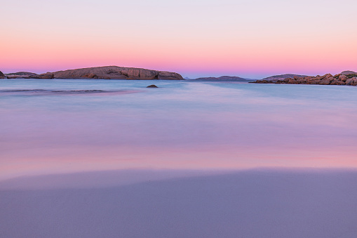 Coastal scene slow shutter captured smooth ocean at dusk reflecting pastel pink skies. Western Australia.