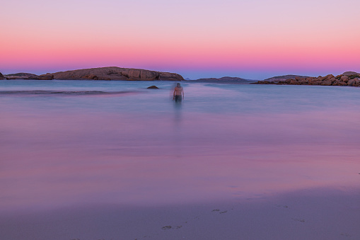 Abstract scene of man standing in smooth ocean at dusk reflecting pastel pink skies. Photographed in Esperance, Western Australia.