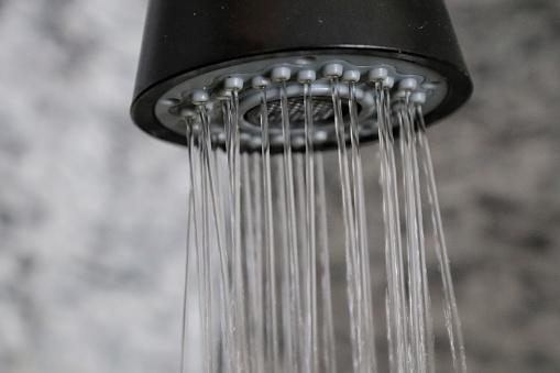 A close-up shot capturing the water stream flowing seamlessly from the nozzles of a showerhead, accentuating the cleanliness and simplicity of a contemporary bathroom setting. The droplets are frozen in mid-air, demonstrating the motion of water during a typical showering experience.