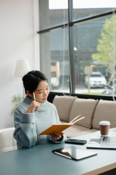 istock Young Asian student studying at the college library, sitting at the desk, using a laptop computer, tablet and headphones having a video chat. 2024650651