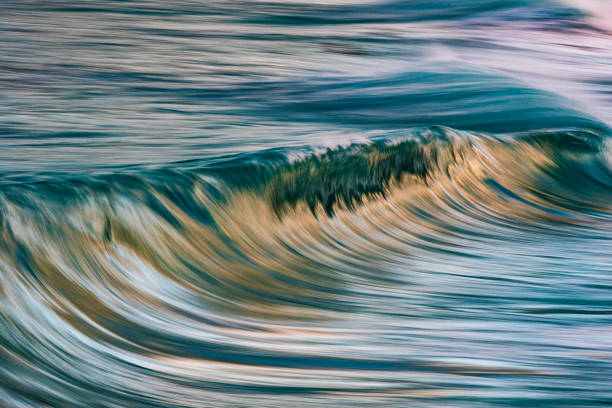istock Slow shutter blur of smooth wave breaking on the beach with ambient soft golden light 2024674399