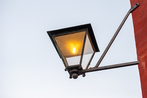 A compact street lamp on a crimson pole near a structure.