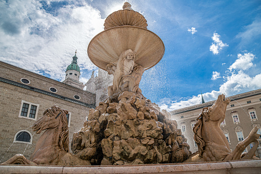 Salzburg: Detail of the medieval Residenzbrunnen, located in Residenzplatz square. In background a view on Residence Palace, famous carillon tower and apse of the Cathedral.
