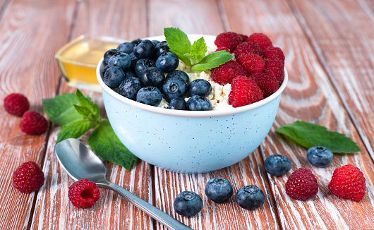A bowl with cottage cheese, ripe berries and honey on the wooden table. Healthy breakfast in the morning. ?lose-up.