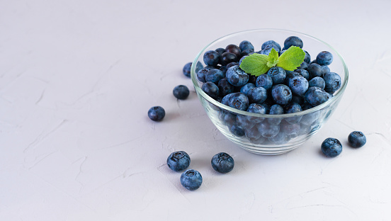 Freshly picked blueberries in a glass bowl on grey background. Close-up. Place for text.