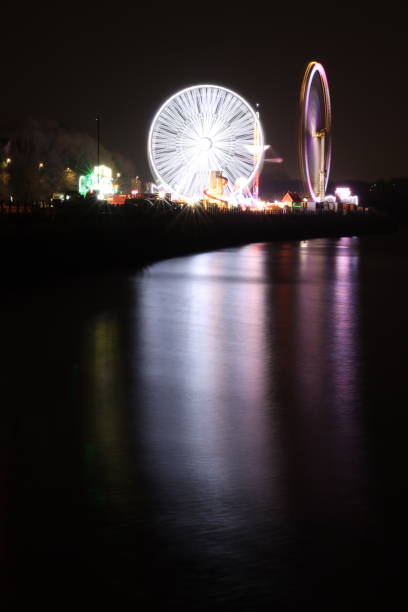 istock Funfair attractions on a city quayside illuminated at night, with multi coloured lights reflected in the water 2024716750