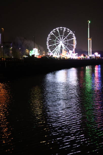 istock Funfair attractions on a city quayside illuminated at night, with multi coloured lights reflected in the water 2024717281