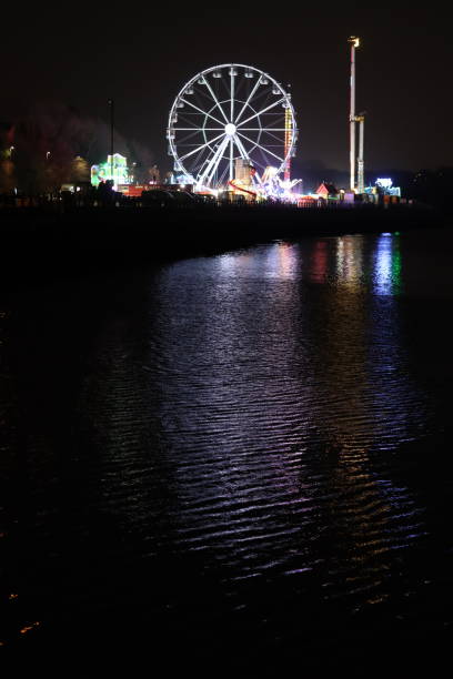istock Funfair attractions on a city quayside illuminated at night, with multi coloured lights reflected in the water 2024718334