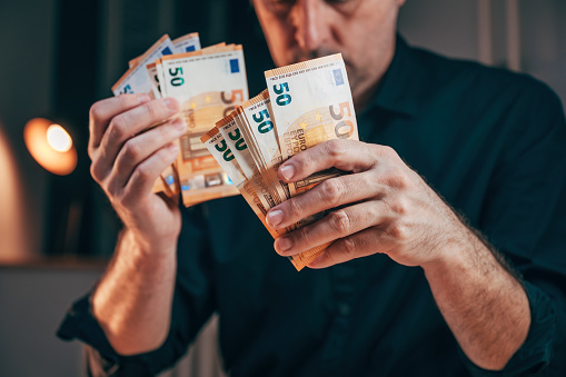 Businessman counting fifty euro banknotes in office while working overtime, selective focus