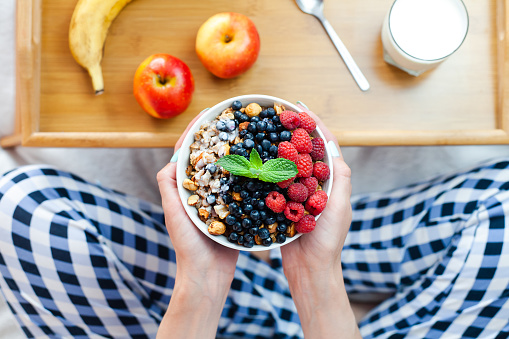 Females hands hold a bowl of granola with fresh with fresh raspberries and blueberries. Healthy breakfast in the morning. ?lose-up. Top view.