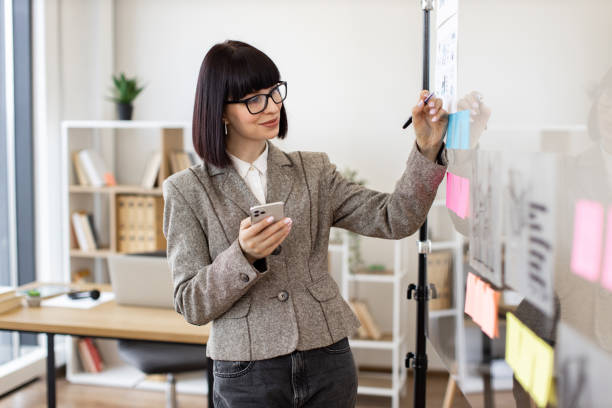 istock Pensive businesswoman typing on phone, writing notes on sticker. 2024722647