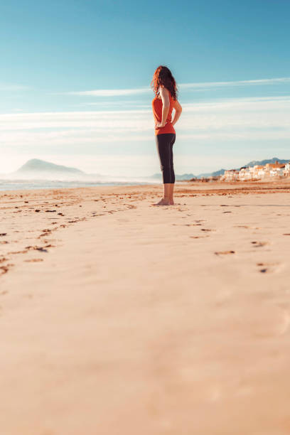 istock woman standing watching horizon on sand of beach 2024729094