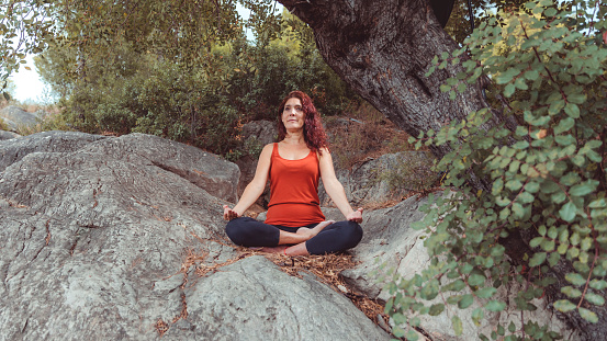 woman in yoga position sitting on some stones under tree in countryside