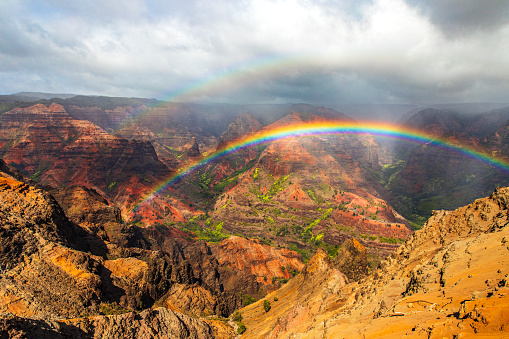 Bright rainbow and mist moving over majestic and colorful mountains and valleys in Hawaii. Photographed in Waimea Canyon, Kauai, Hawaii.