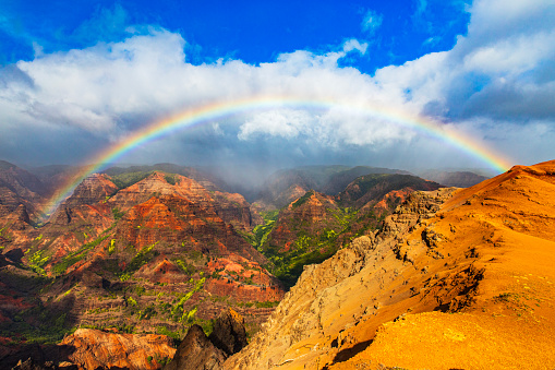 Bright rainbow and mist moving over majestic and colorful mountains and valleys in Hawaii. Photographed in Waimea Canyon, Kauai, Hawaii.