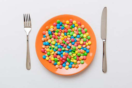 cutlery on table and sweet plate of candy. Health and obesity concept, top view on colored background.