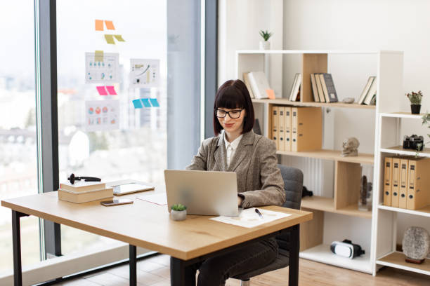 istock Lady in suit and eyeglasses sitting comfortably at table with laptop computer. 2024764910