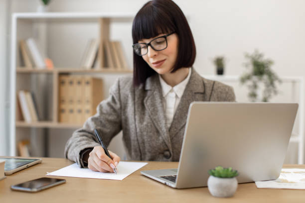 istock Woman in eyeglasses making notes with pen while looking at laptop screen. 2024764914