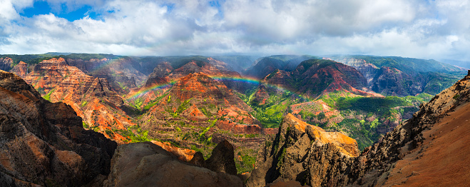 Panorama of rainbow and mist moving over majestic and colorful mountains and valleys in Hawaii. Photographed in Waimea Canyon, Kauai, Hawaii.