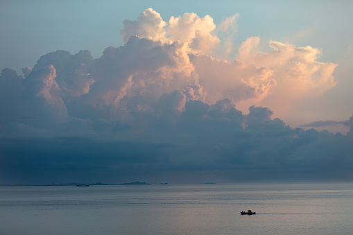 High storm clouds gather over the mountains and southern coast of Corsica, seen from the Sardinian side of the Strait of Bonifacio. A small fishing boat, dwarfed by the huge clouds, crosses the placid waters of the sea.