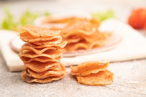 Slices of dehydrated salted meat chips with herbs and spices on gray concrete background and white textile. Side view, close up, selective focus