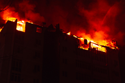 Huge fire blazing in multi storey apartment building. Burning house is engulfed in flames at night during the disastrous