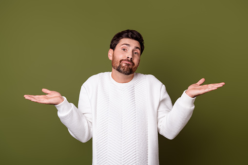 Photo of uncertain unsure man wear trendy clothes shrugging shoulders no answer isolated on khaki color background.