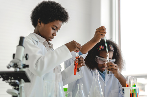 Two african american cute little boy and girl student child learning research and doing a chemical experiment while making analyzing and mixing liquid in test tube at science class on the table.Education and science concept