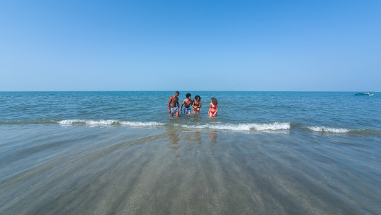 friends stand in shallow waters of the sea, with gentle waves lapping around them under a vast blue sky.