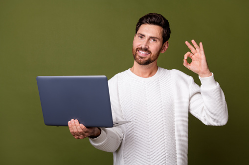 Foto de un atractivo gerente de hombre contento que anuncia un dispositivo moderno netbook macbook okey letrero aislado sobre fondo de color caqui photo