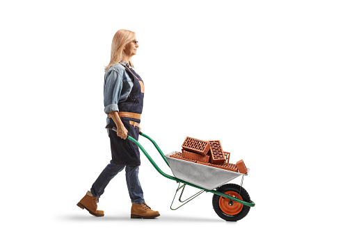 Full length profile shot of a woman pushing a wheelbarrow full of bricks isolated on white background