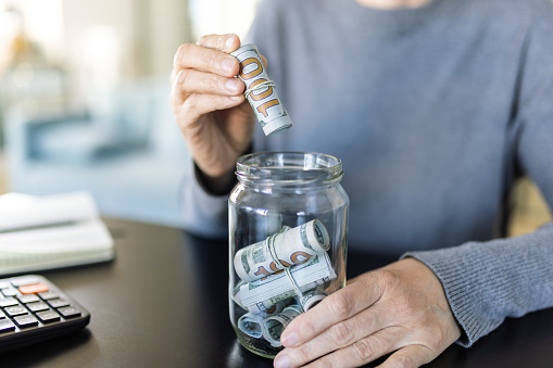 A woman putting rolled up US dollar bills into a glass jar.