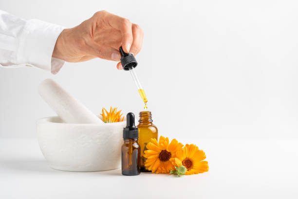 calendula flowers in mortar, amber glass bottles with essential oil and pharmacist hand with pipette. - pot marigold single flower flower flower head ストックフォトと画像