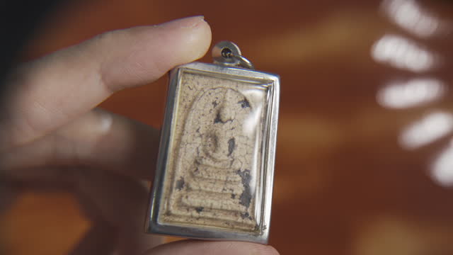 Using a magnifying glass to see the detail on an old Thai Buddha amulet